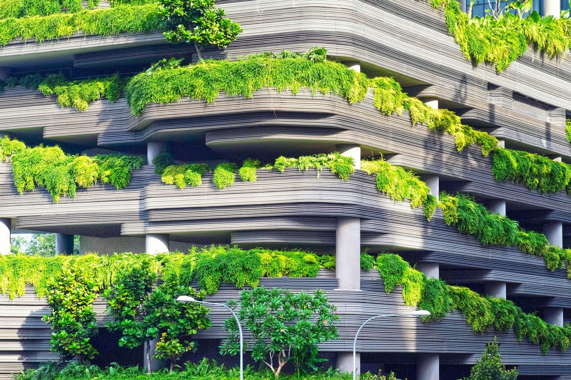 Detailed view of a modern building with layered, undulating concrete balconies covered in dense green foliage and tropical plants.