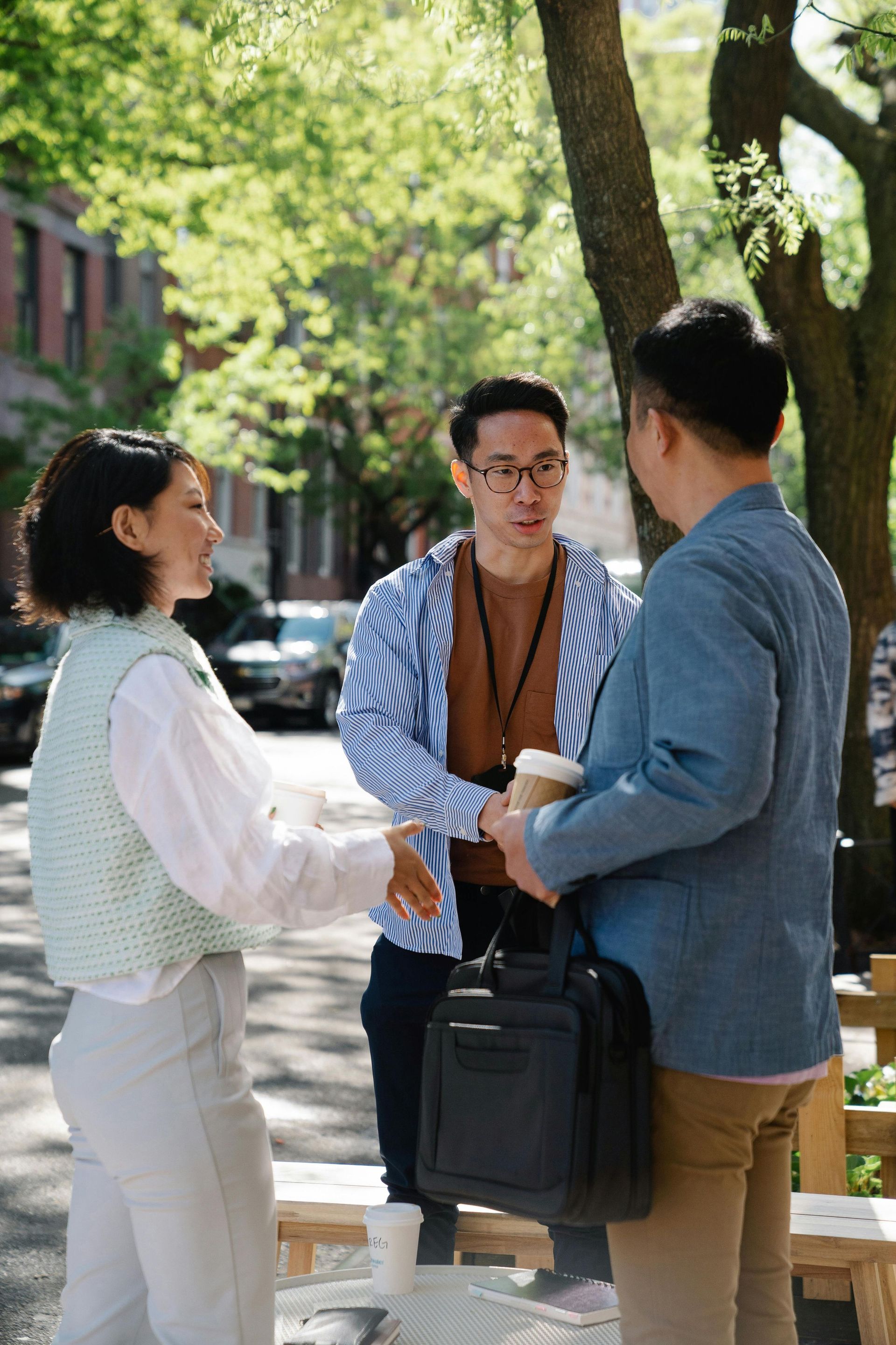 Three business professionals having a conversation and shaking hands outdoors in a park-like setting.