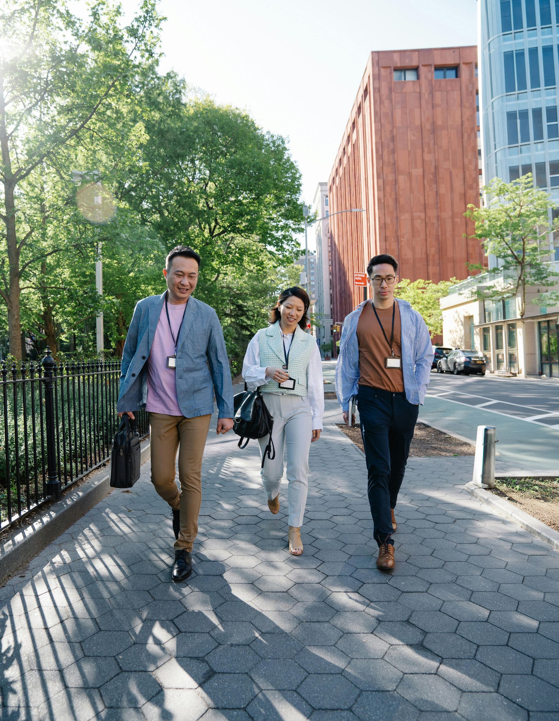 Three people wearing ID lanyards walking together on a paved path in an urban park.